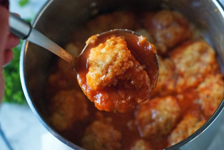 a ladle with tomato soup and dumplings on it