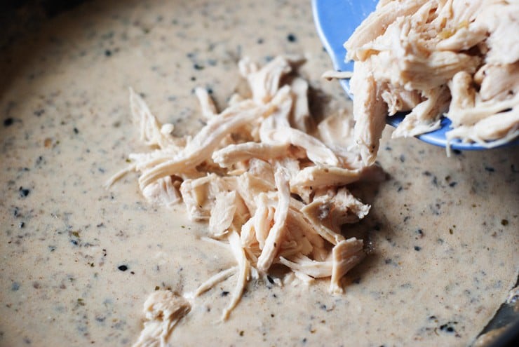 Chicken being poured into sour cream enchilada sauce