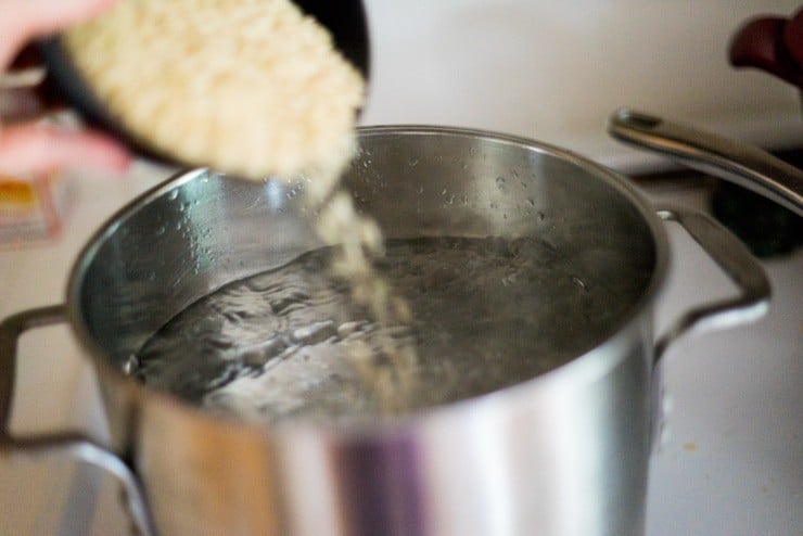 Pouring brown rice into a pot of boiling water to cook