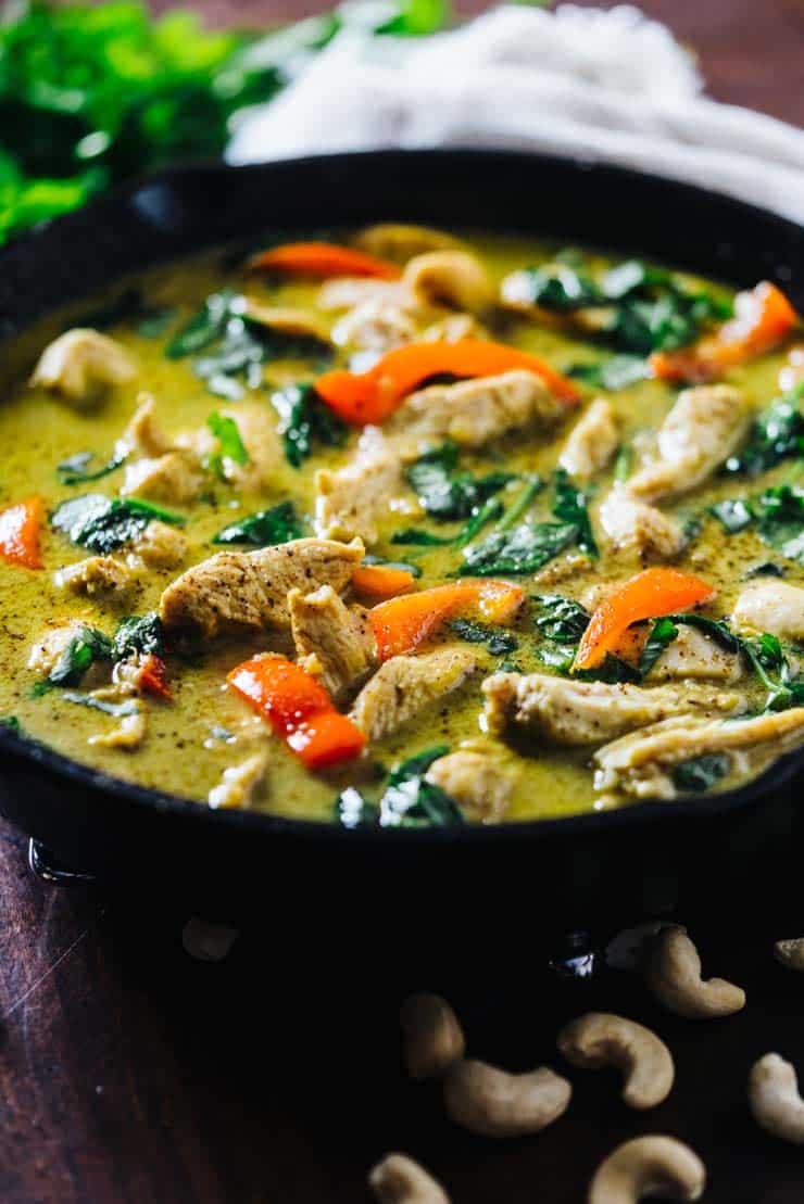 Chicken curry made with coconut milk with spinach and peppers in a cast iron skillet
