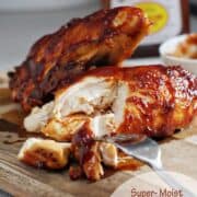 BBQ chicken cut on a cutting board with a bottle of bbq sauce