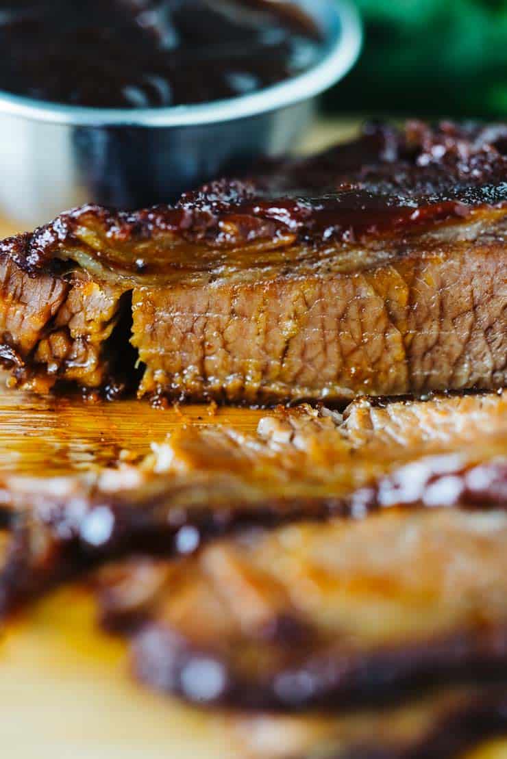 sliced instant pot brisket on wood cutting board with cup of sauce in background