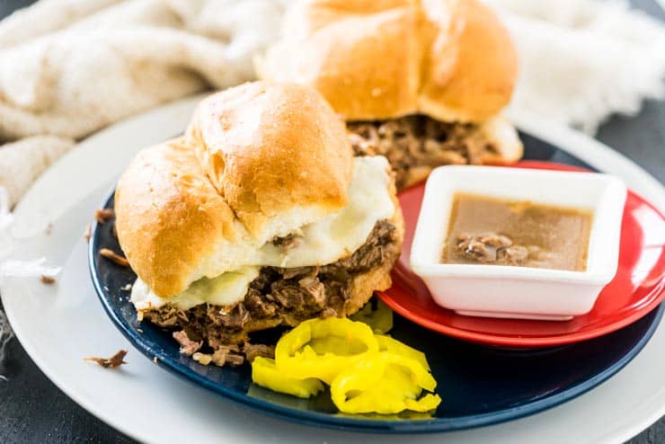 2 crock pot shredded italian beef sandwiches on a plate with au jus