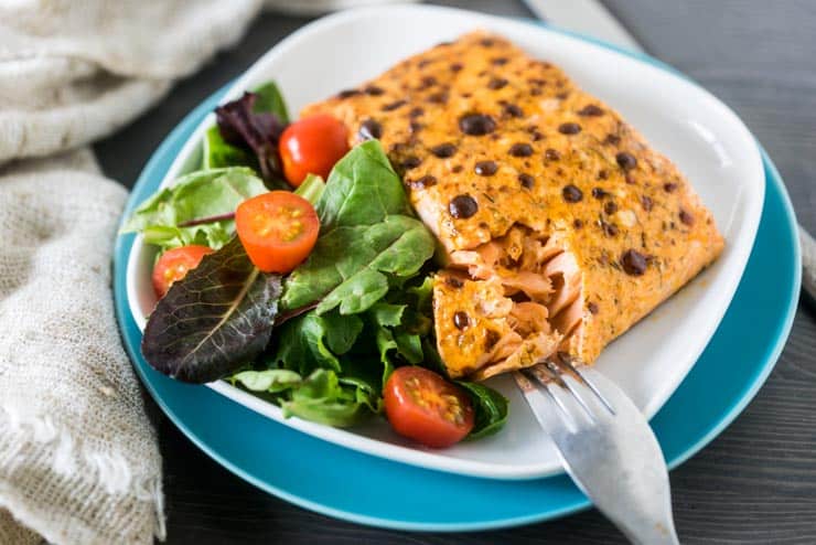 Broiled Salmon Fillet on white and blue plates with greens and tomatoes