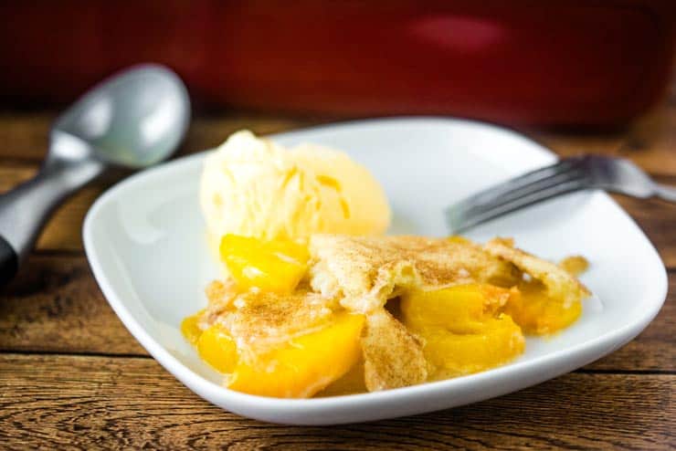 Scoop of snickerdoodle peach cobbler on a white plate with a fork and ice cream scooper.