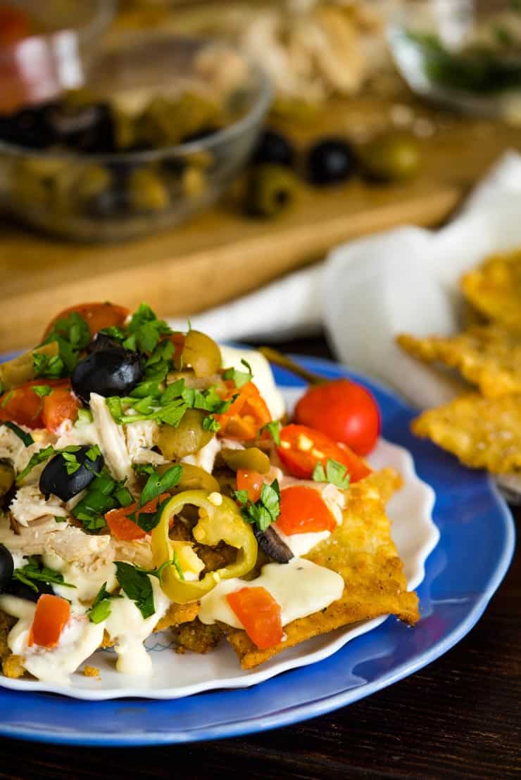 Italian Nachos on a blue plate with alfredo sauce, olives and cherry peppers.