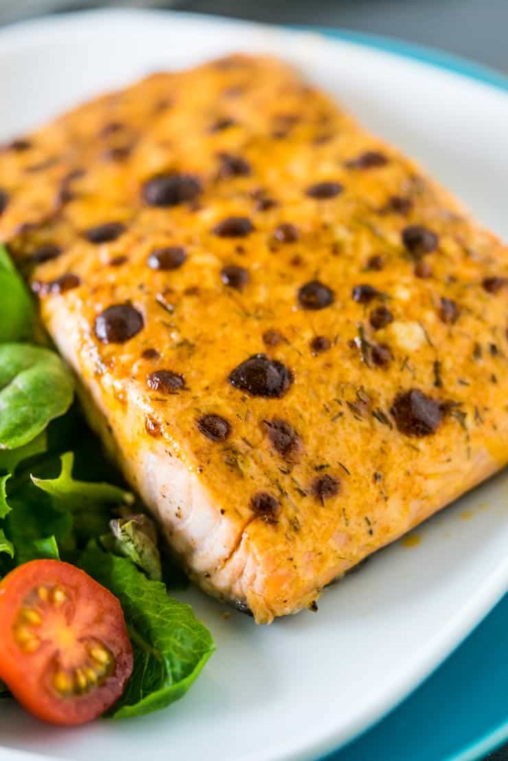 Piece of broiled salmon on a white plate with salad