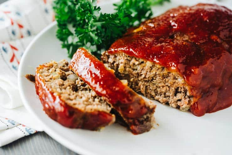 Sliced meatloaf on a white plate with ketchup glaze