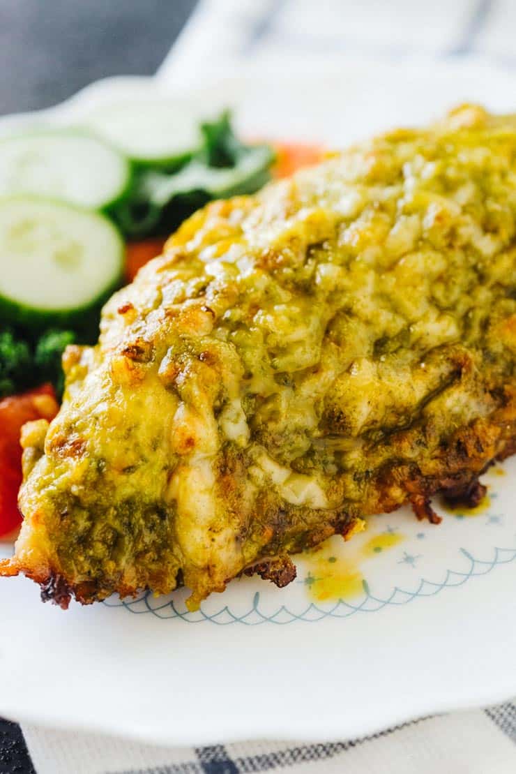 A Baked Pesto Chicken Breast on a white plate with a side salad