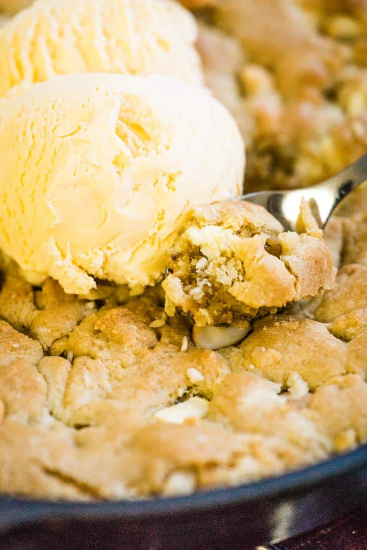 Spoonful of baked pizookie with white chocolate and macadamia nuts. Topped with vanilla ice cream.
