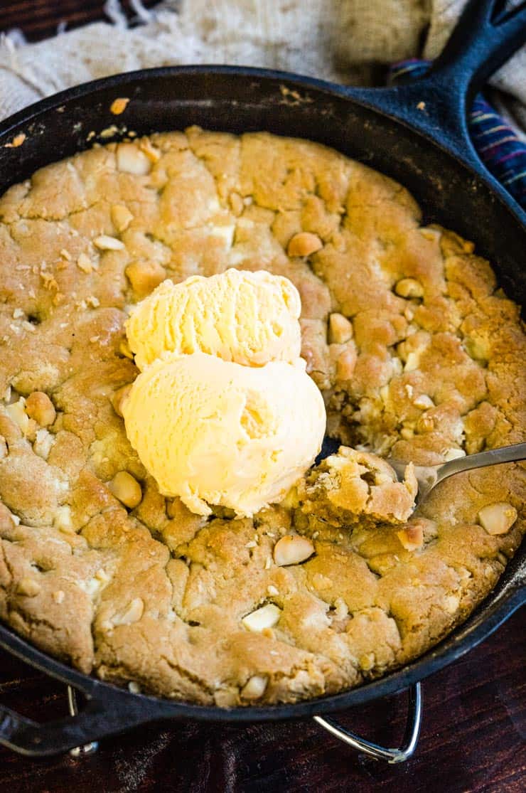 A White Chocolate Macadamia Nut Pizookie in a cast iron skillet with vanilla ice cream on top