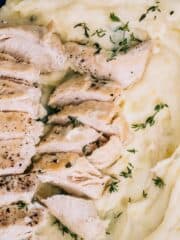 Sliced chicken and herbs on top of mashed potatoes