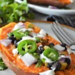 half sweet potato on a plate with onion, jalepeno, black beans and cheese