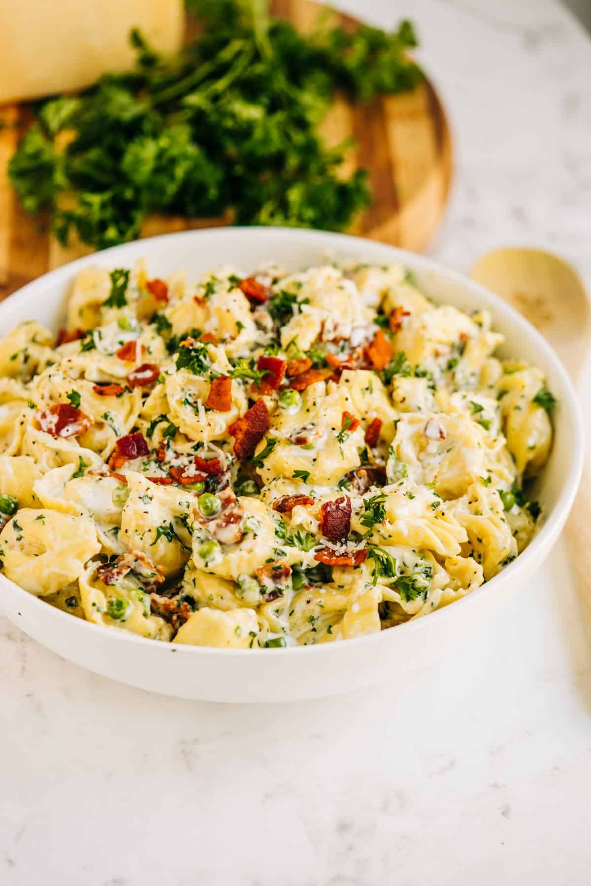 Creamy tortellini in a white bowl with bacon and peas